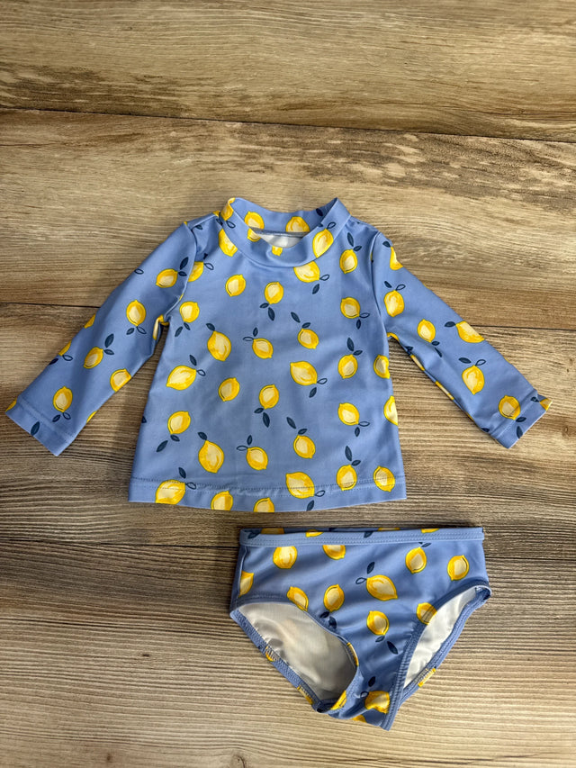 Flat lay of 2-piece blue lemon-print rashguard and bikini bottoms showing long sleeves and yellow lemons on wooden floor