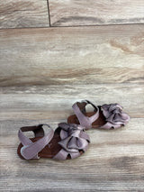 Front three-quarter view of EYY mauve baby sandals showing large bow detail and Velcro ankle straps on wood background