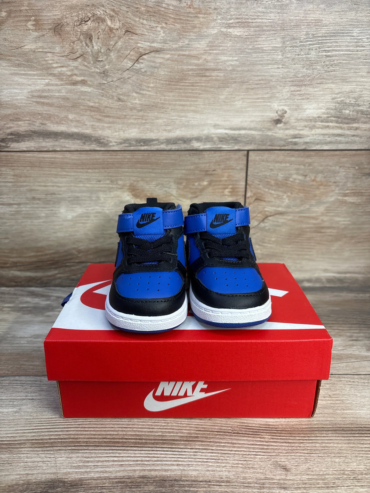 Front view of toddler Nike Court Borough Mid 2 sneakers in black and game royal with Velcro strap on red Nike box