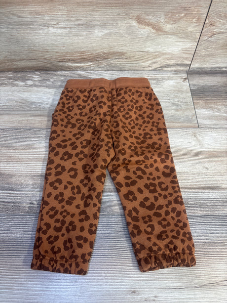 Flat lay of brown leopard print Okie Dokie jogger pants showing elastic waistband and cuffed ankles on light wood background