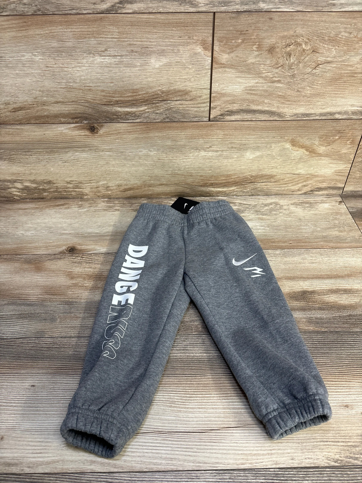 Flat lay of grey toddler Nike joggers (2T) showing white DANGER text, Nike swoosh, elastic waistband and cuffs on wood floor
