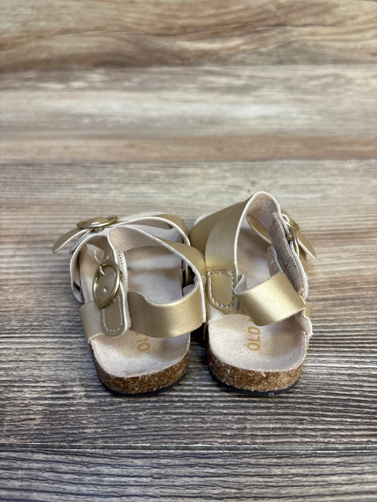 Gold toddler sandals with cork soles and buckles on wooden floor