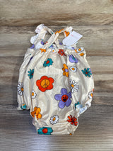 Flat lay of beige floral crossback baby romper showing crisscross straps, elastic leg openings and colorful flower print on wood