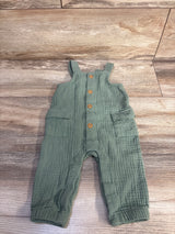 Flat lay of green Cat and Jack gauze button jumpsuit (3-6 mo) showing front buttons and patch pockets on wood floor