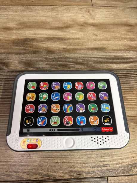 Front view of Fisher Price Laugh & Learn Smart Stages Tablet showcasing alphabet buttons and numbered switch on a wood surface