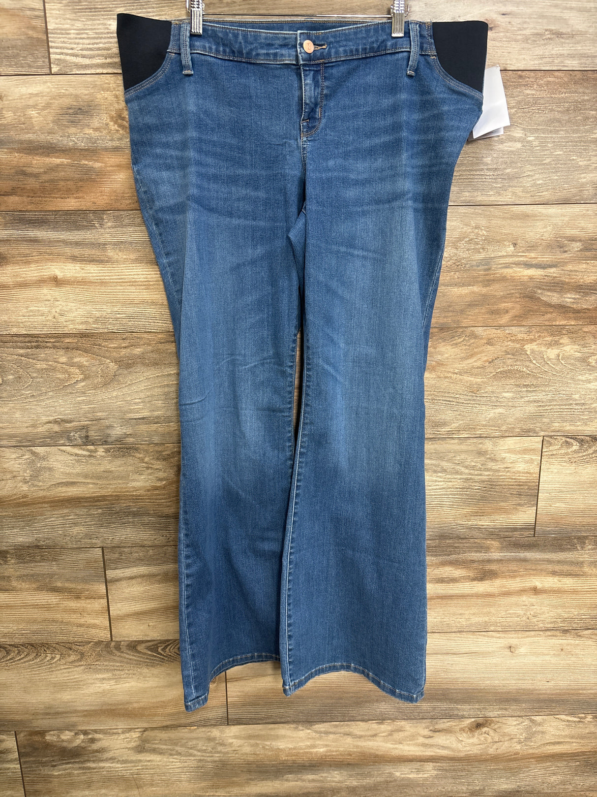 Front view of blue Isabel maternity flare jeans showing black side stretch panels and flared legs on wood background