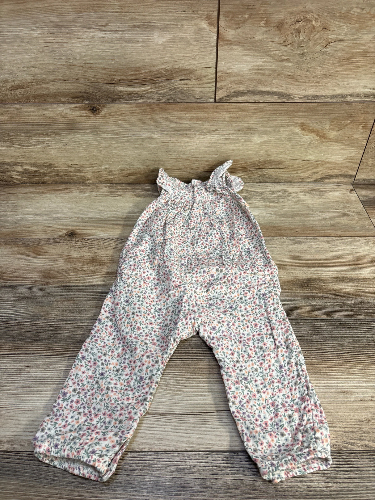Flat lay of white smocked floral baby jumpsuit 12 months showing ruffled straps and elastic cuffs on wood background