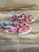 Angled view of Limited Too pink slip-on sneakers showcasing front bow and rainbow print on wood background