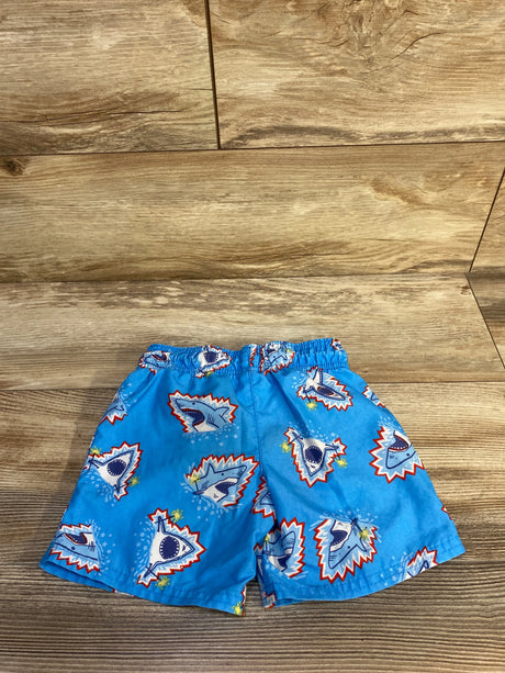 Flat lay of blue Cat & Jack swim trunks showcasing cartoon shark print and elastic waistband on wood floor background