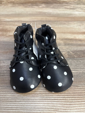 Black baby shoes with white polka dots and black laces on wooden surface