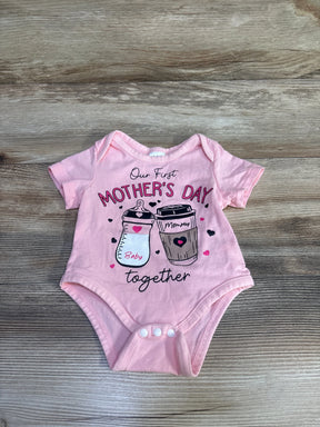 Flat-lay of pink 0-3M bodysuit showing 'Our First Mother's Day' print with baby bottle and coffee cup on wood background