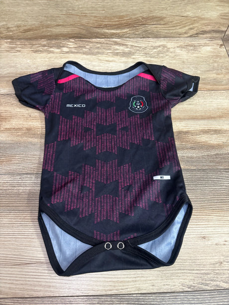 Front view of black Mexico soccer jersey bodysuit showcasing red geometric pattern, crest, and snap closures on wood flooring
