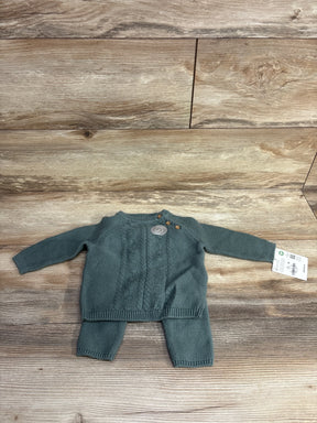 Green knit baby sweater and pants set with wooden buttons, displayed on wood floor