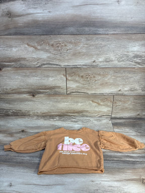 Tan kids' sweatshirt with 'be nice' text on wood background