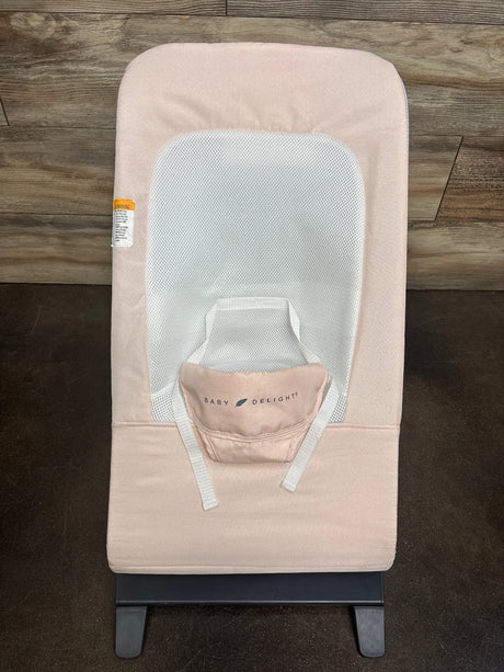 Top-down view of Baby Delight Alpine Deluxe bouncer in light pink showing white mesh seat insert, safety straps, and black base on wood floor