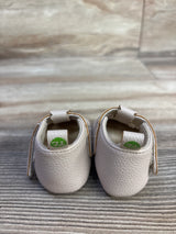 Rear view of First Steps soft sole shoes in beige showing textured leather, heel loops and Velcro straps on wood backdrop