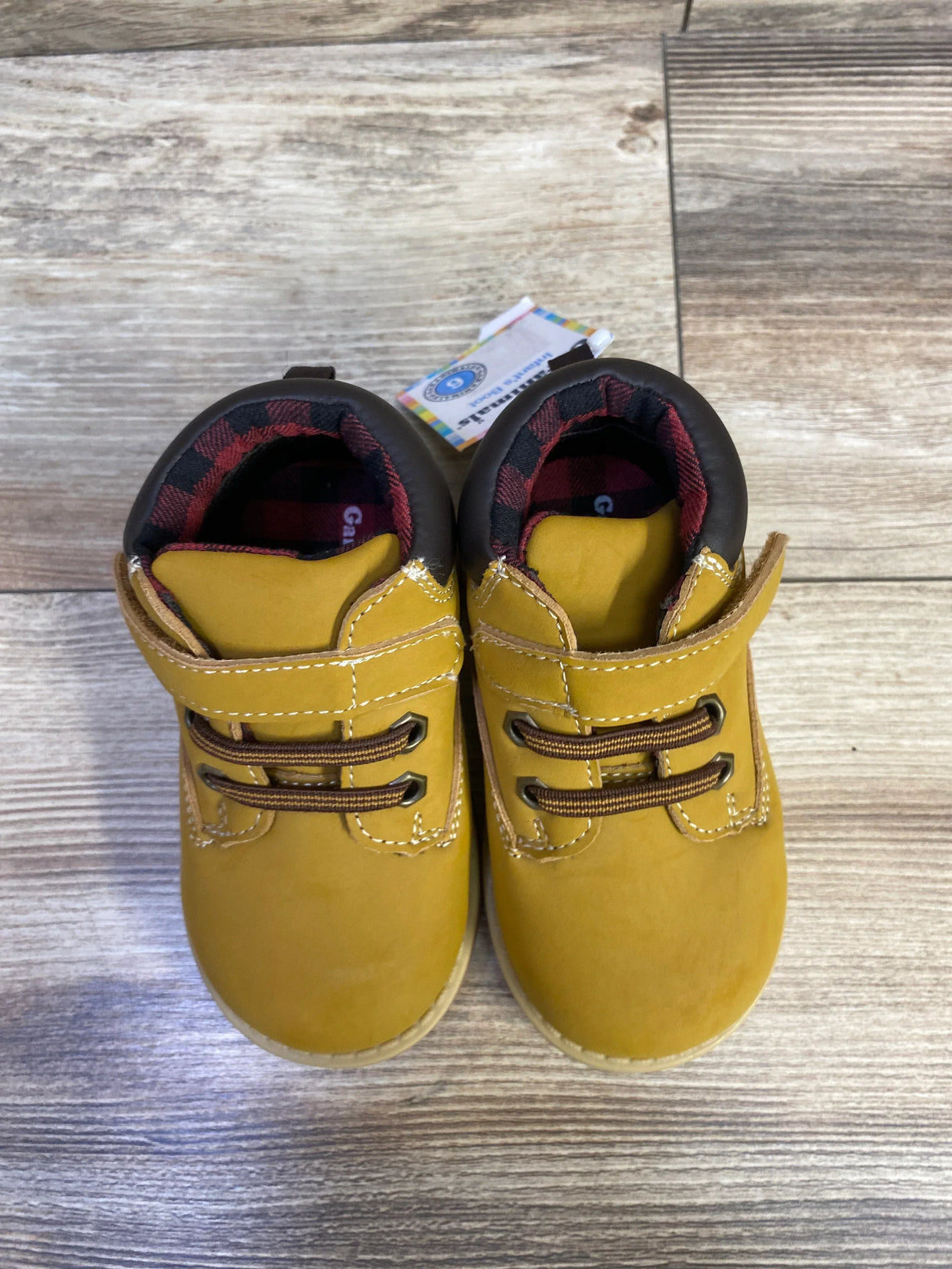 Top-down view of toddler tan Garanimals boots with Velcro strap, faux brown laces and red plaid lining on wood floor