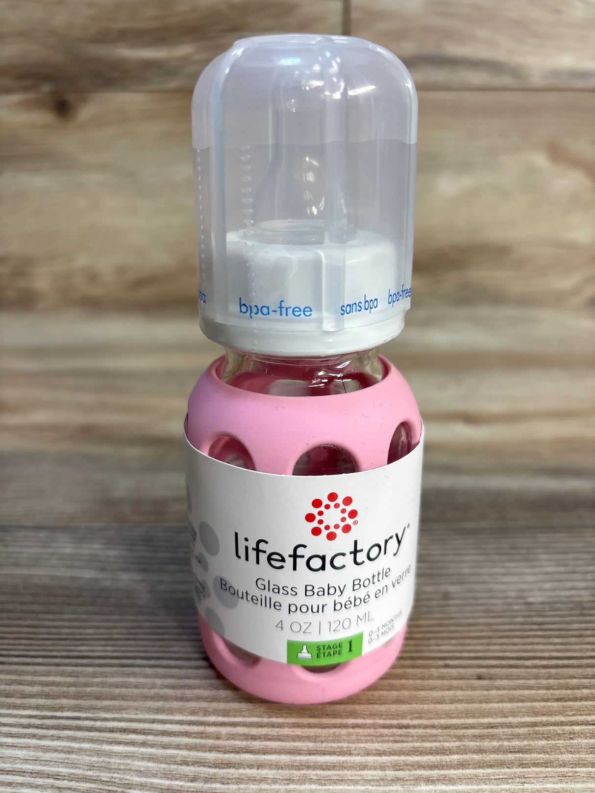 Lifefactory glass baby bottle with pink silicone sleeve and BPA-free cap on wood background