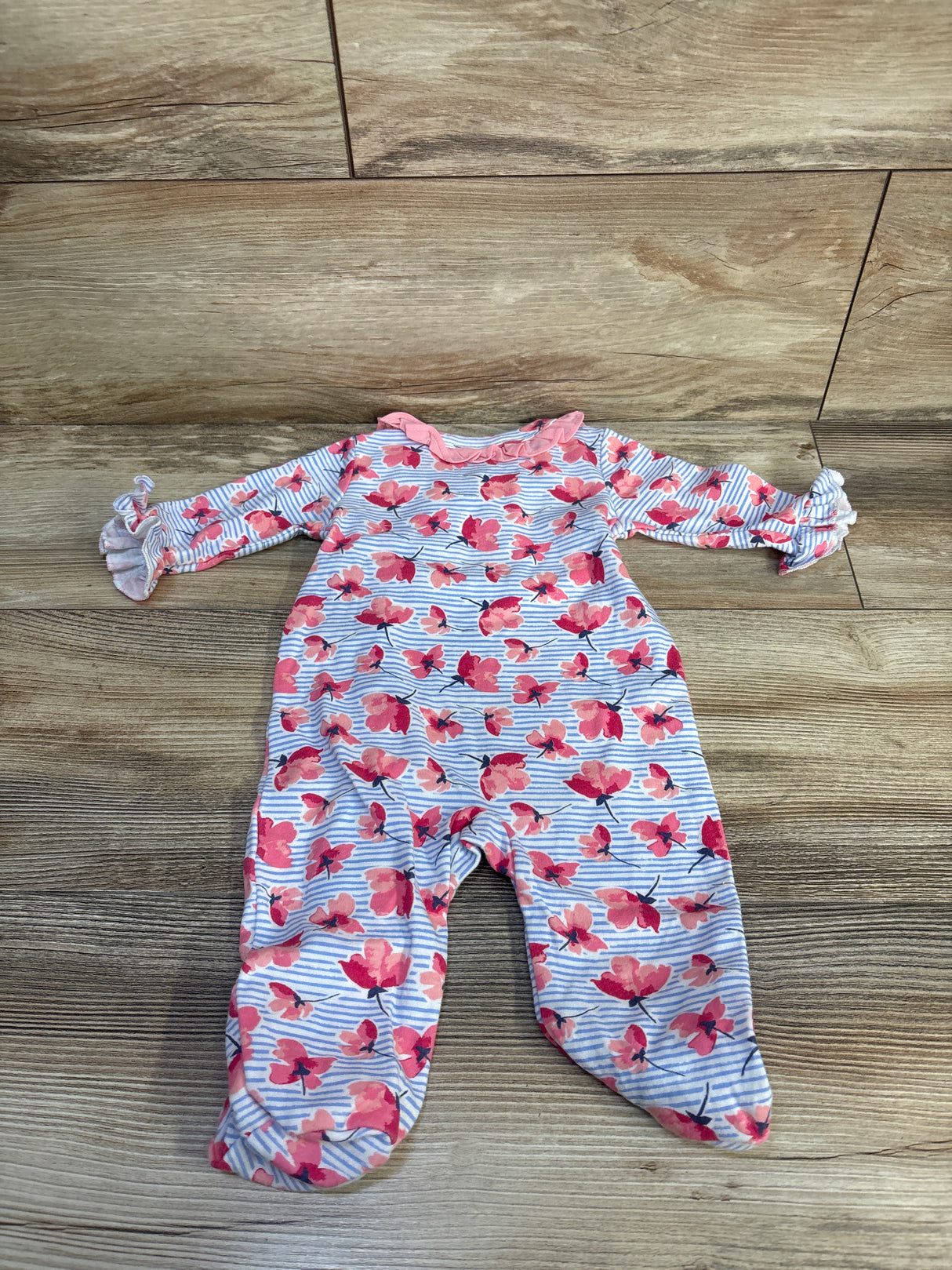 Flat lay of Nicole Miller blue floral footed baby coverall, size 3-6M, showing ruffle collar and ruffled sleeve cuffs on light wood floor background