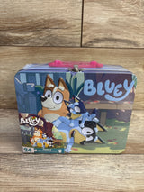 Front view of Bluey 24pc jigsaw puzzle tin lunchbox showing Bluey artwork, pink handle and metal latch on wooden table