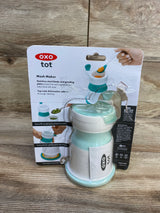 Front view of OXO Tot Mash Maker baby food mill in opal showing lid and suction base in original blister pack on wood table