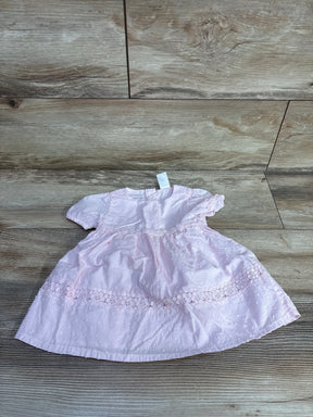 Front flat lay of OshKosh baby dress showcasing pink Swiss dot fabric and floral eyelet lace trim with wood plank background