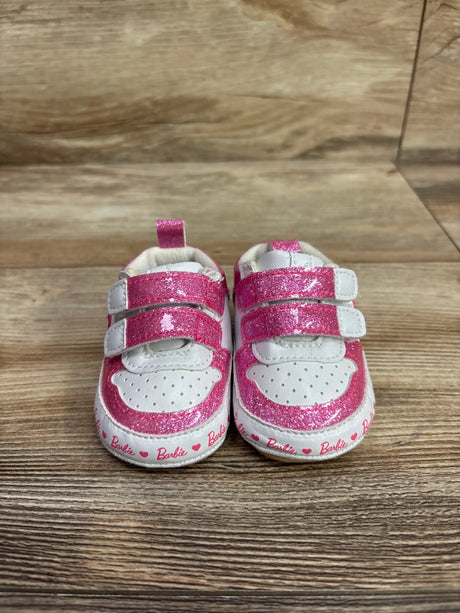 Front view of Barbie soft sole sneakers with pink glitter uppers, white trim, and two straps on a wood-grain surface
