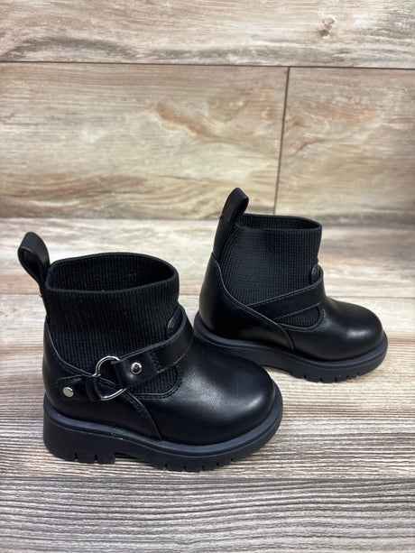 Front view of Baby Gap Heart moto boots in black size 4C showcasing buckle straps and lug soles on a wood look background