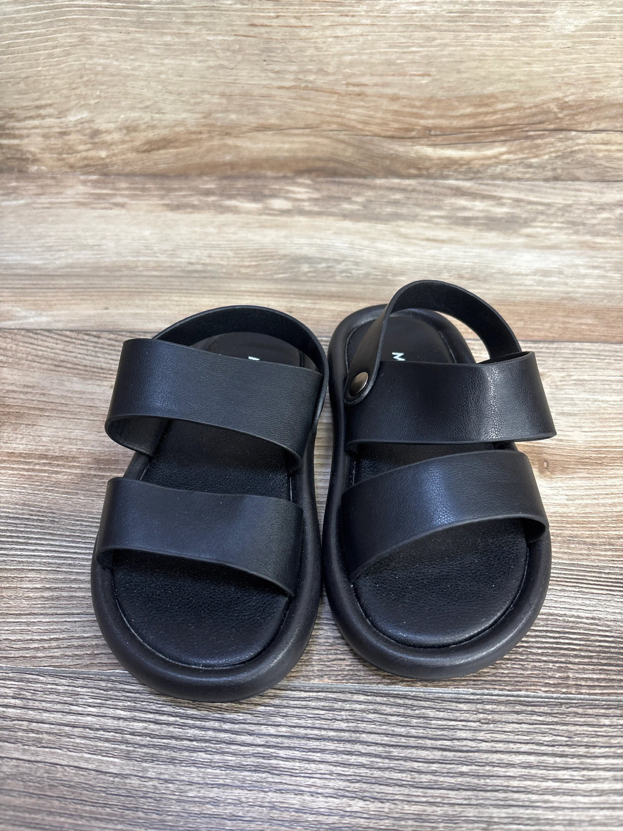 Front view of MGBABY black foam toddler sandals with two wide straps, snap heel strap, cushioned sole on wood background