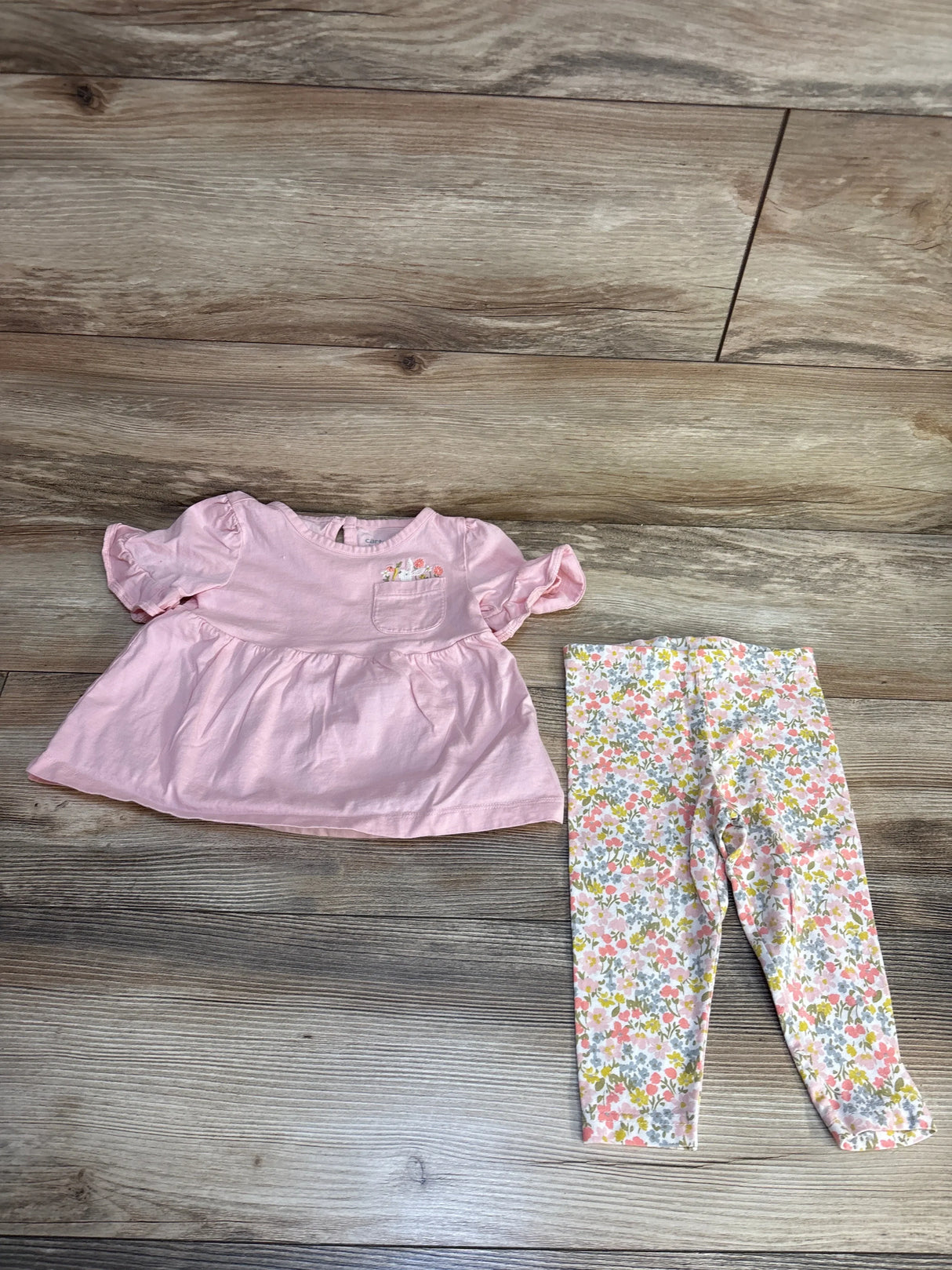 Pink baby top with floral pocket and matching floral leggings on wood floor