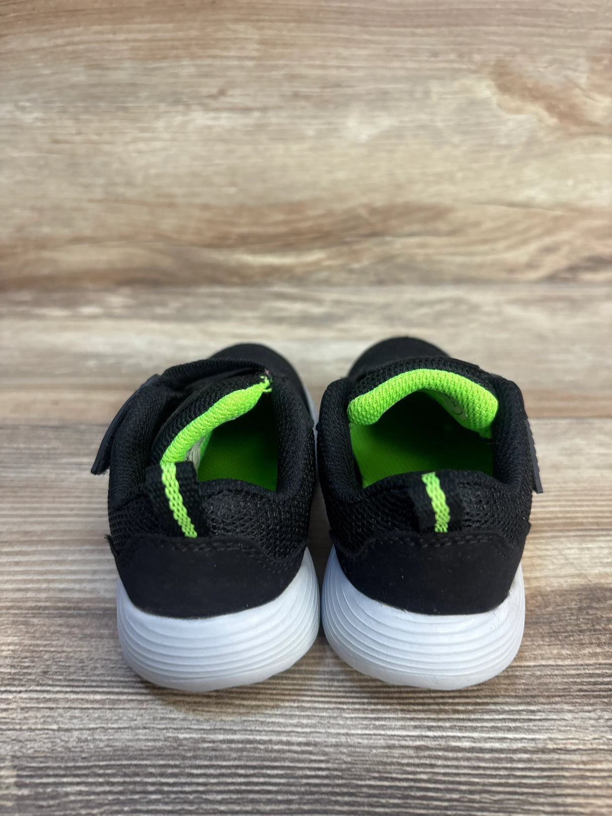 Black and green toddler athletic shoes with white soles on wood background