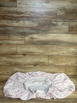 Top-down view of The Peanutshell fitted crib sheet in white with pink and gray floral print and elastic edge on wood floor