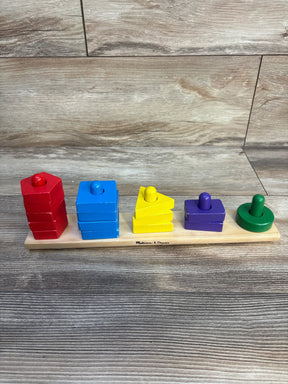 Front view of Melissa & Doug Stack and Sort Board showcasing five colorful shape stacks on a light wood base and wood-panel background
