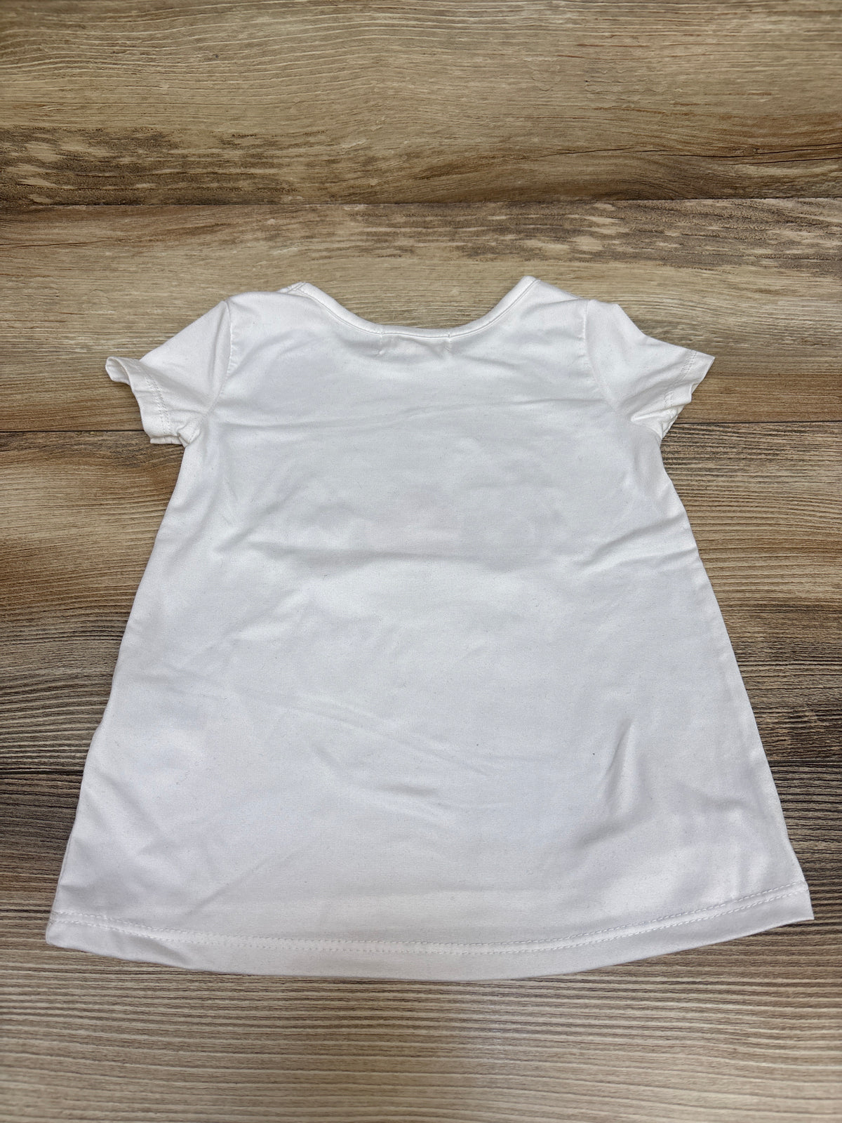 Back view of Btween unicorn shirt in white, size 2T, showcasing its short sleeves and plain back on a wood surface