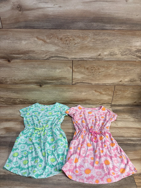 Flat lay of two toddler floral dresses, green and pink, showing daisy print and elastic cinched waists on wood floor