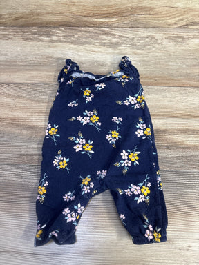 Flat-lay of navy floral sleeveless newborn jumpsuit showing ruffled shoulder straps and snap crotch on wood background
