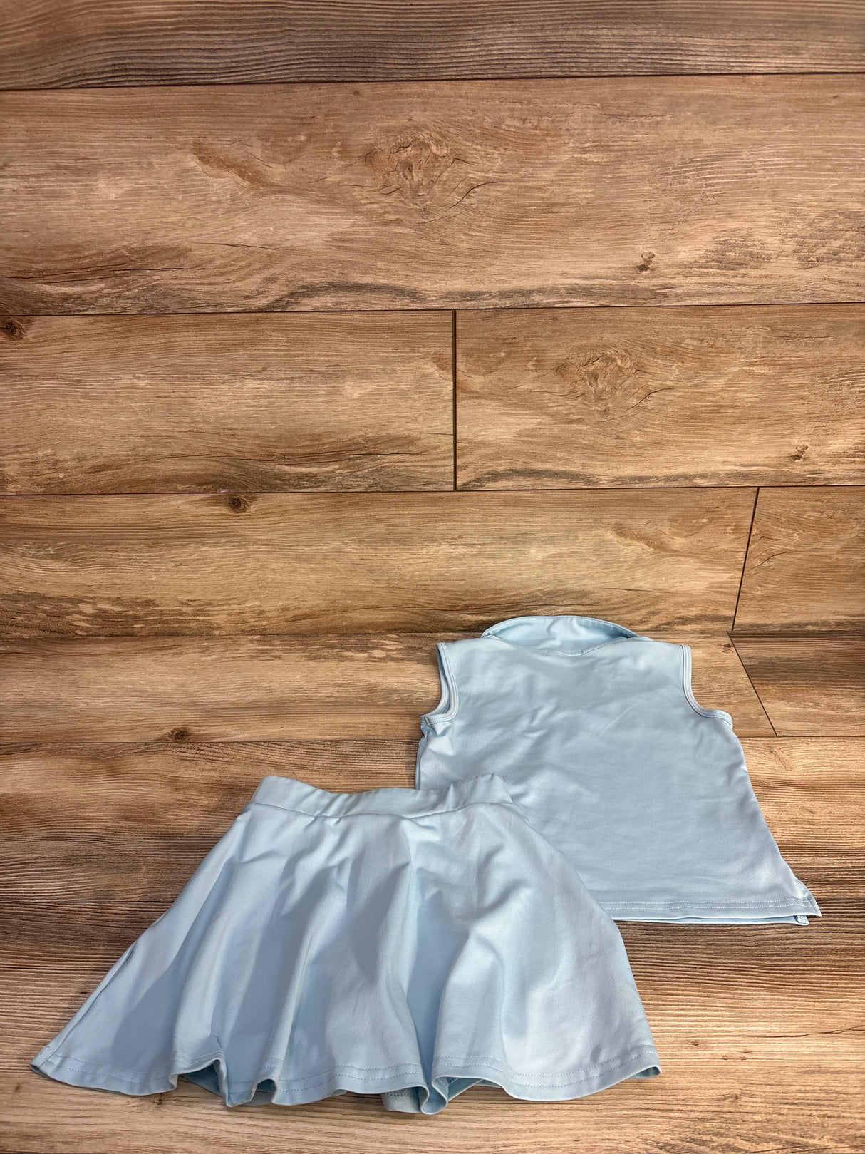 Laid-flat view of girls' light blue 2-piece tennis outfit (collared sleeveless top and flared skort) size 5T on wood floor