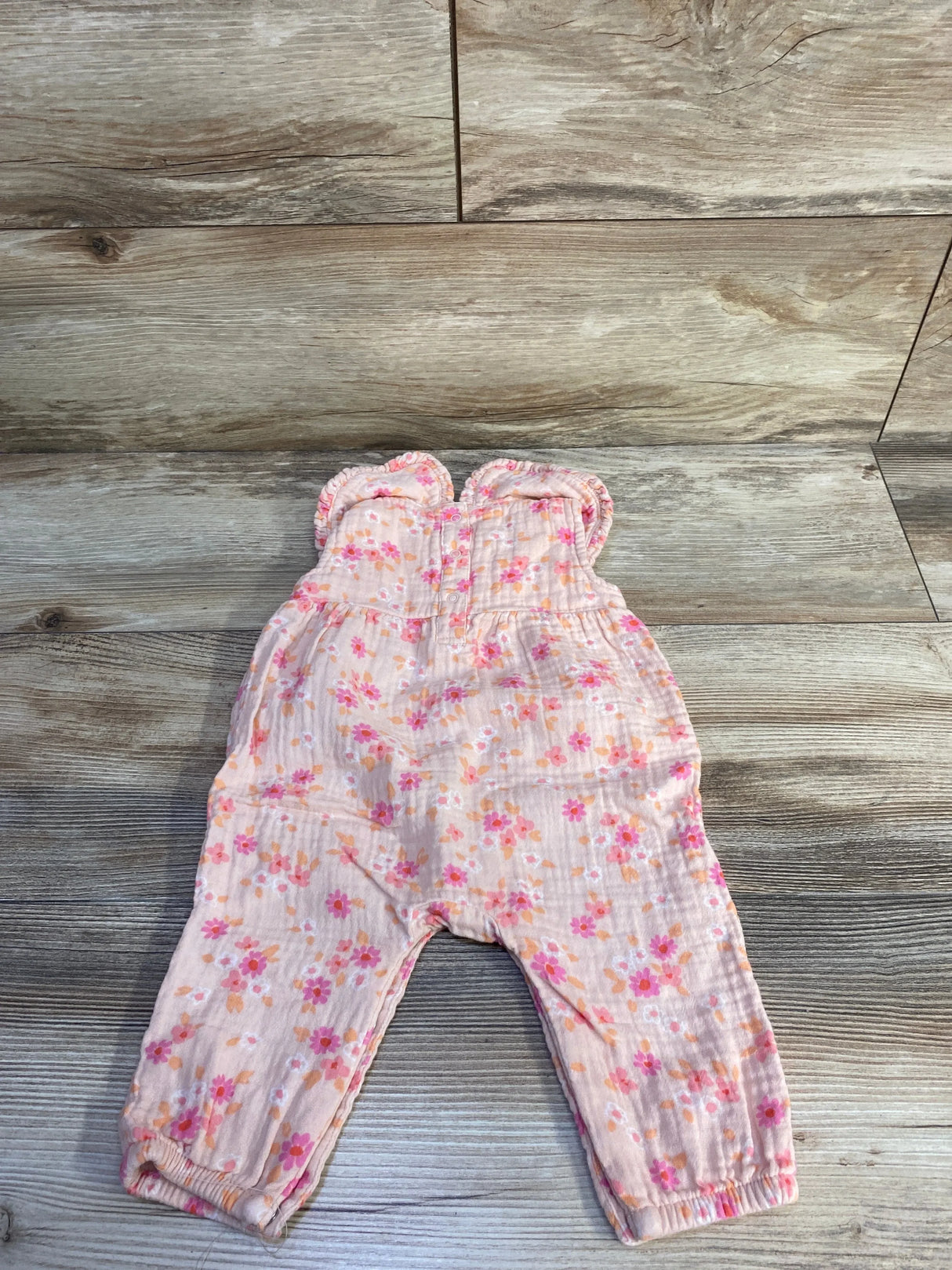 Flat lay of pink Cat and Jack gauze jumpsuit with collared top, ruffle straps, floral print and elasticized ankles on wood background