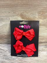 Front view of two red grosgrain ribbon hair bows on black branded card against wood background