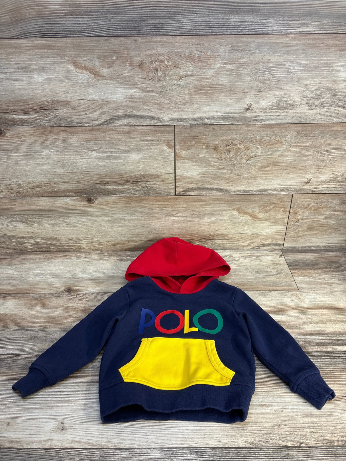Navy blue kids hoodie with red hood, yellow pocket, and colorful POLO logo, laid on wood floor