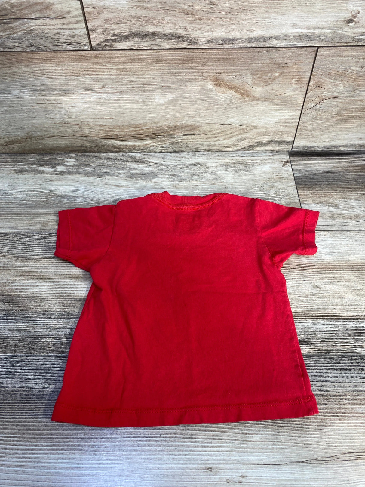 Back view of red Paw Patrol toddler t-shirt (size 2T) showing plain back and short sleeves on wood background