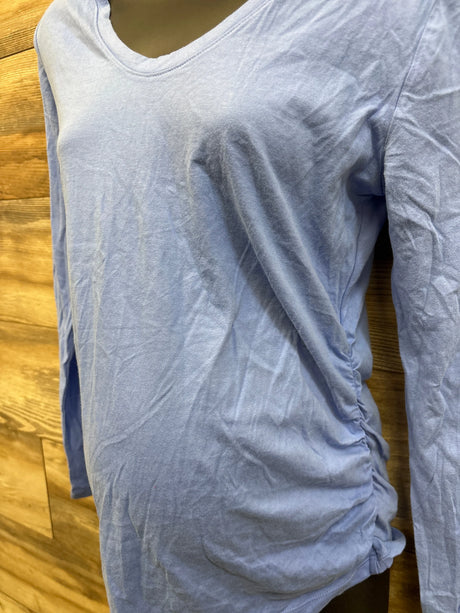 Three-quarter view of maternity long sleeve top in blue showing side ruching over belly on mannequin with wood background