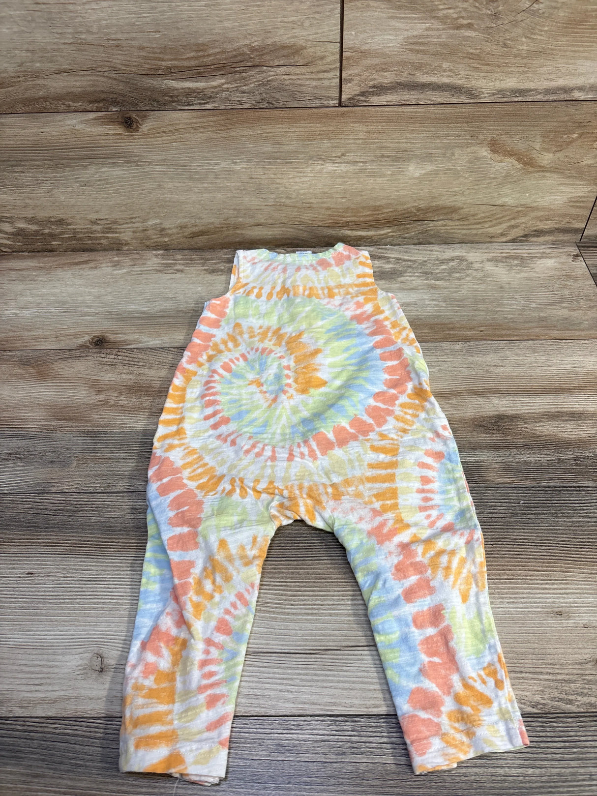 Front flat-lay of Old Navy sleeveless tank romper in pastel spiral tie-dye showing orange, yellow and blue swirls on wood floor