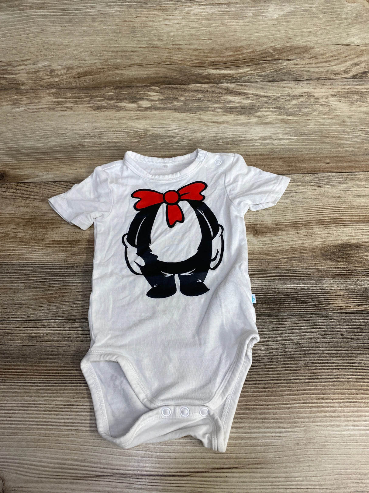 White baby onesie on wooden surface with cartoon design of black character wearing red bow