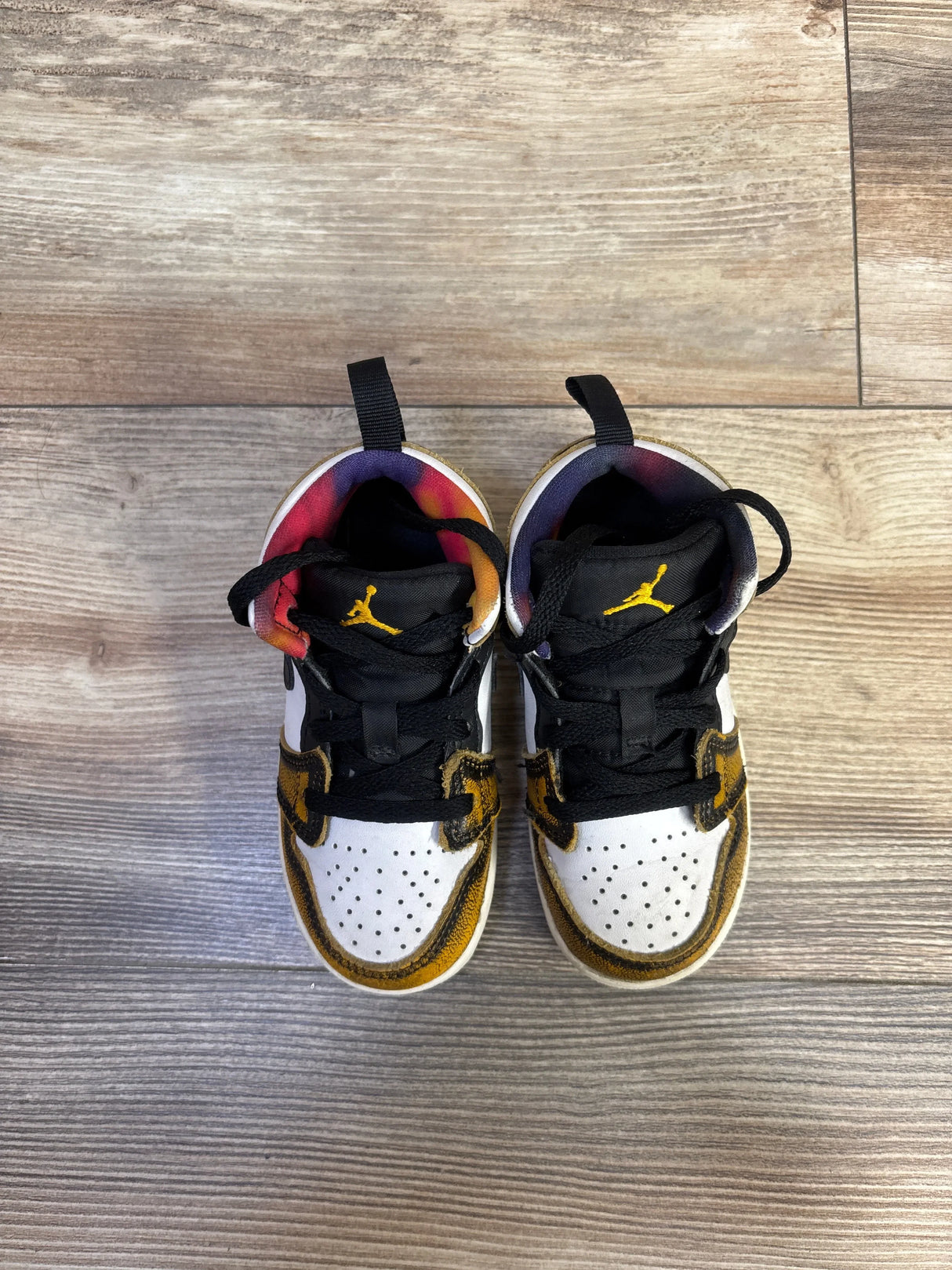 Top view of Air Jordan 1 Mid TD Wear-Away Taxi toddler sneakers showing yellow overlays, black laces and Jumpman on wood floor