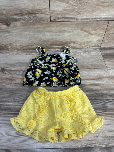 Flat lay of Little Lass 2-piece lemon-print gem top and yellow lace ruffle shorts on wood background