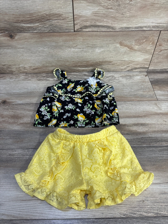 Flat lay of Little Lass 2-piece lemon-print gem top and yellow lace ruffle shorts on wood background