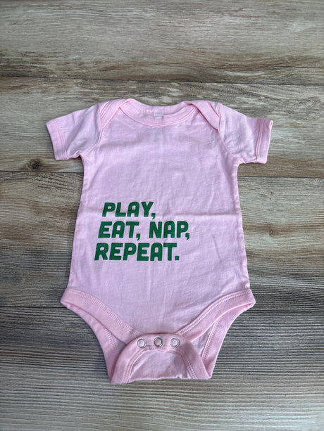 Pink baby onesie with green text Play, Eat, Nap, Repeat on wood background