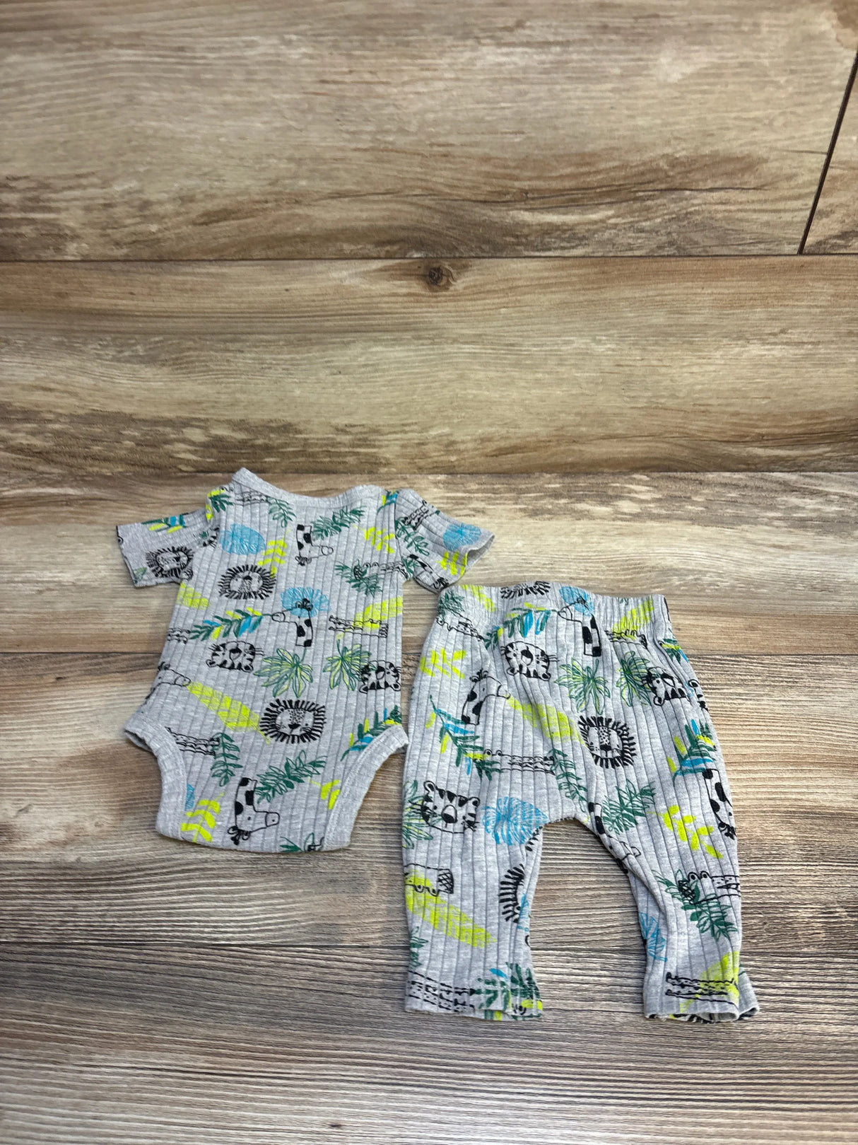 Gray baby onesie and pants set with animal and leaf print on wood background