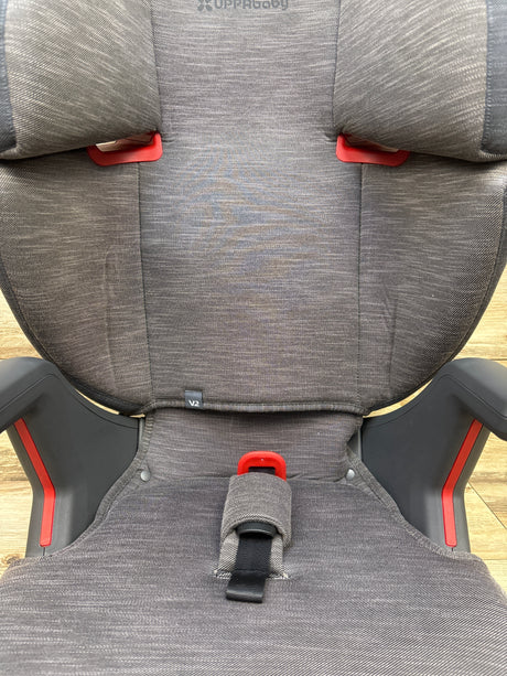 Front view of UPPAbaby Alta V2 High Back Booster Car Seat in Greyson showcasing gray upholstery and red side accents on a wood floor